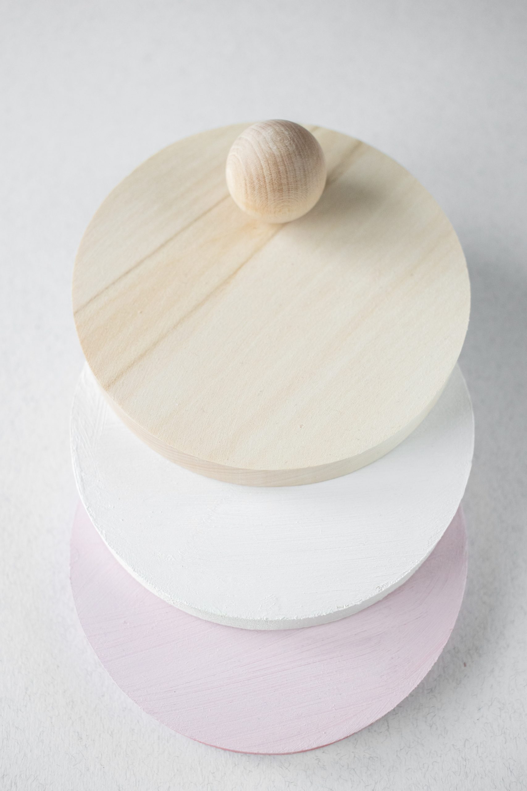 three flat wooden circles in wood, white and pink